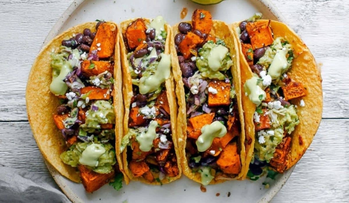 Black bean and sweet potato tacos on a plate with lime wedges and avocado crema