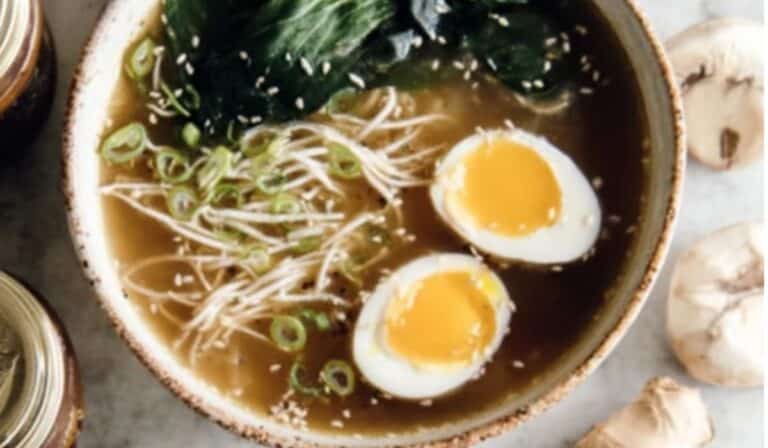 Gut-healing bone broth ramen bowl with egg, bok choy, and mushrooms on a wooden table